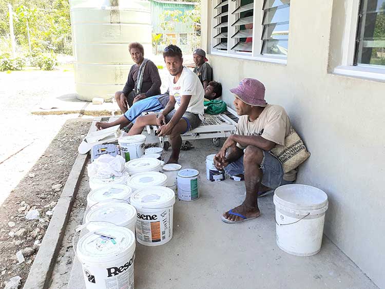 Five Solomon island mean taking a break from painting in the shade of the clinic. Large buckets of paint in the foreground.